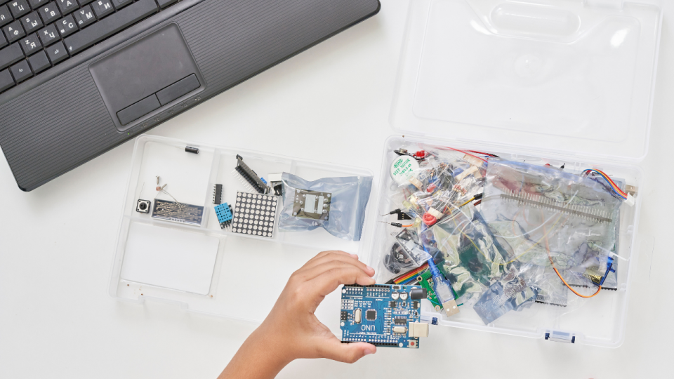 Young student holding an Arduino from a box of electronic parts