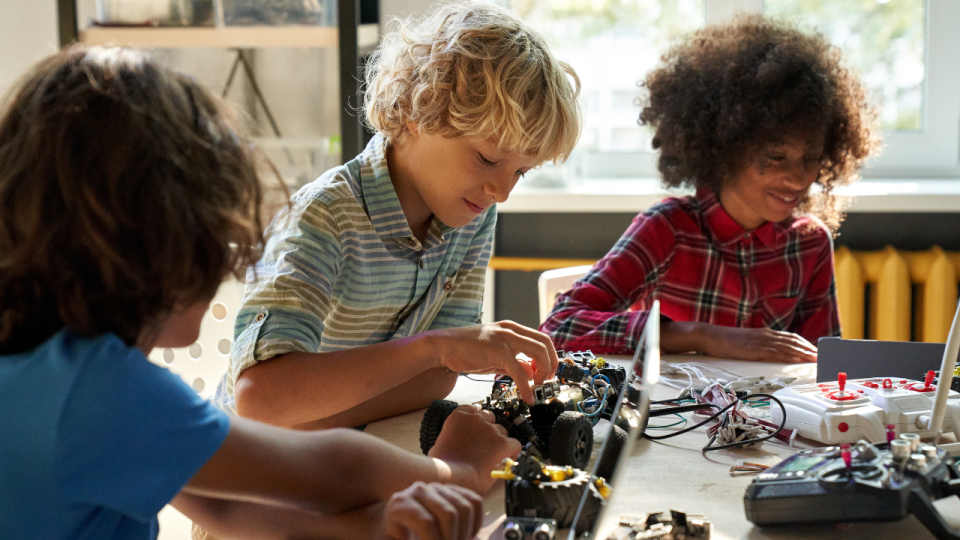Three boys working together to assemble and program a robotic car