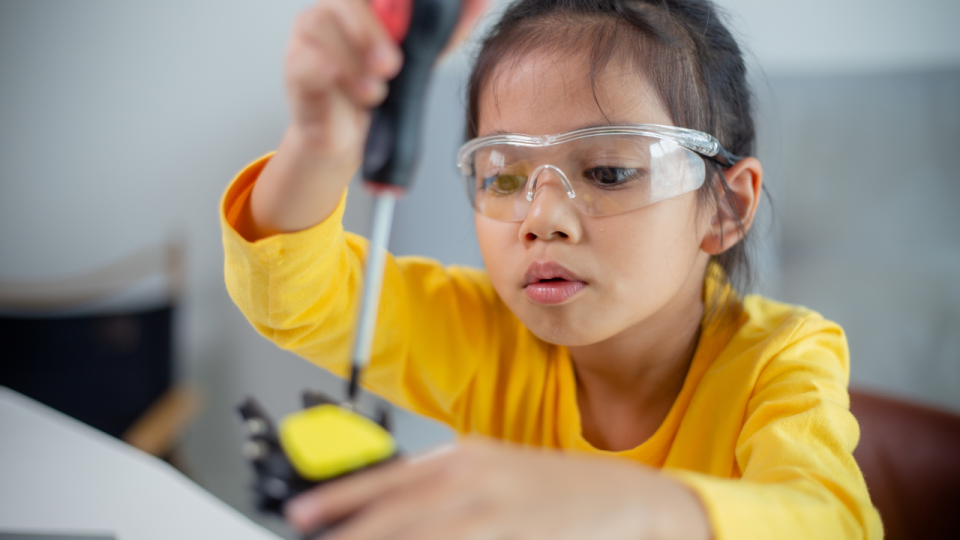 Young girl wearing safety glasses and using a screwdriver to assemble something mechanical